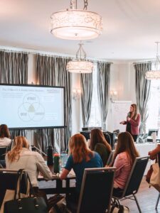 Business Coach Laura Schoenfeld in front of audience talking about how to create a high-ticket coaching program
