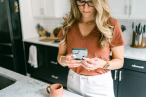 Business Coach Laura Schoenfeld holding phone image used in blog about How to Get High-Paying Clients as a Health Coach